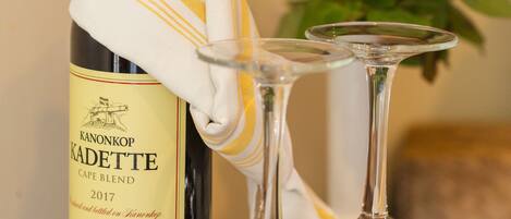 A bottle of Kanonkop Kadette wine with two empty wine glasses on a table.