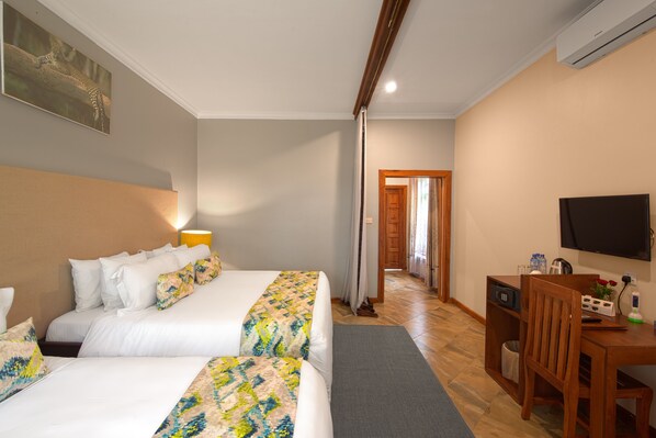 A hotel room with two beds, a desk, a television, and a door leading to a hallway.
