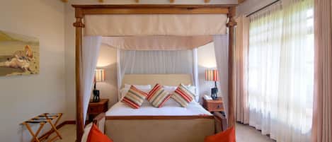 A four-poster bed with a canopy, two bedside tables with lamps, a wooden folding chair, and a painting on the wall.