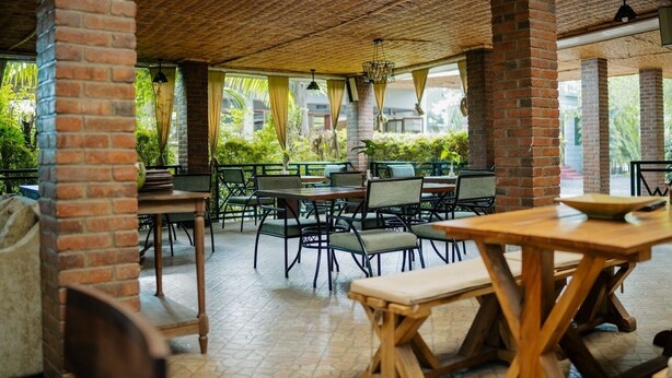 Un café al aire libre con pilares de ladrillo, mesas y sillas de madera.