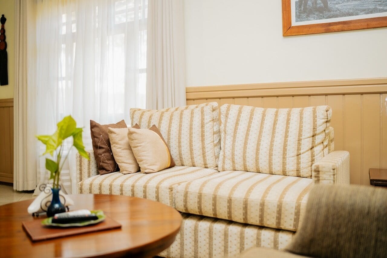 A striped sofa with a wooden headboard, a small table with a remote control, and a plant.
