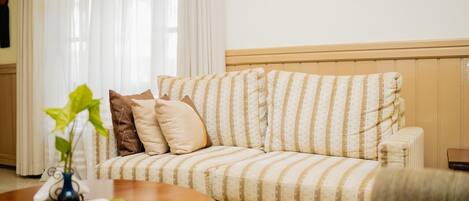 A striped sofa with a wooden headboard, a small table with a remote control, and a plant.