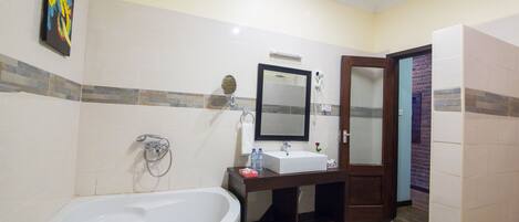 A bathroom with a bathtub, a sink, a mirror, and a door leading to another room.