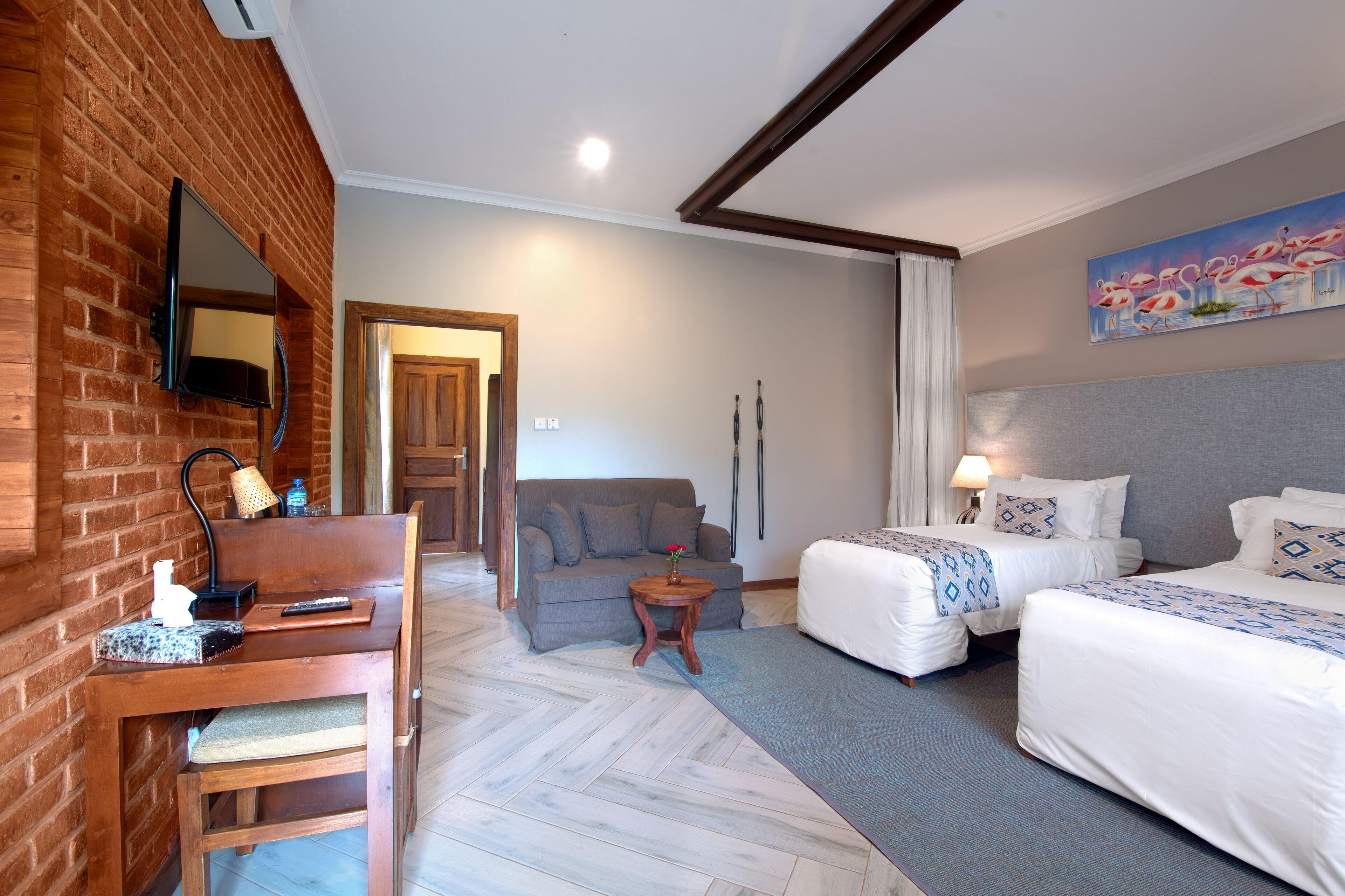 Habitación de hotel con pared de ladrillo, un sofá, dos camas, una mesita y un cuadro.