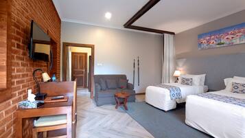 A hotel room with a brick wall, a sofa, two beds, a small table, and a painting.