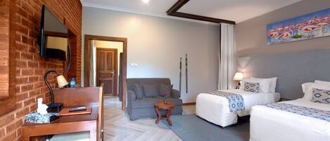 Habitación de hotel con pared de ladrillo, un sofá, dos camas, una mesita y un cuadro.