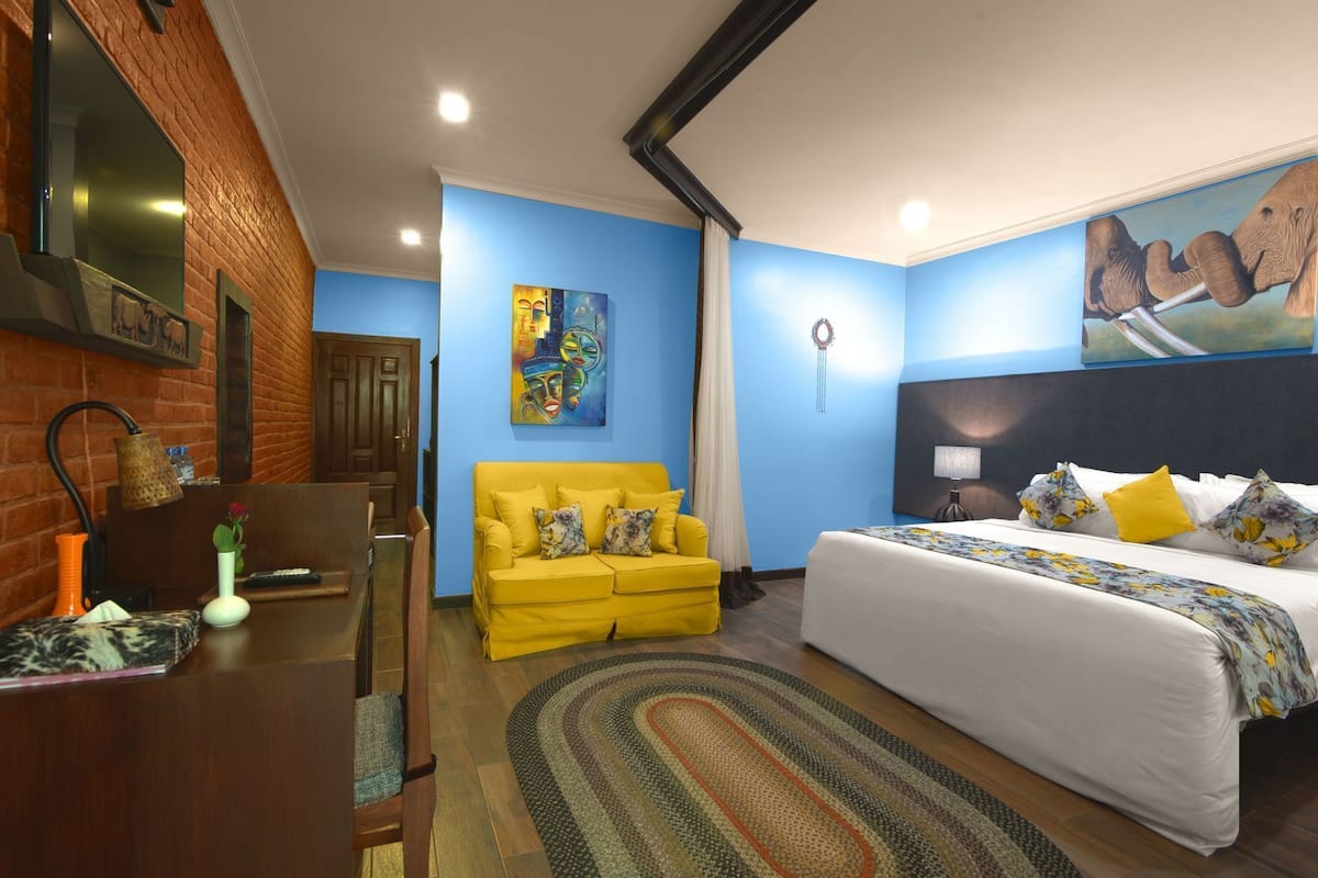 Una habitación de hotel con una cama, un sillón amarillo, un escritorio con lámpara y un cuadro en la pared.