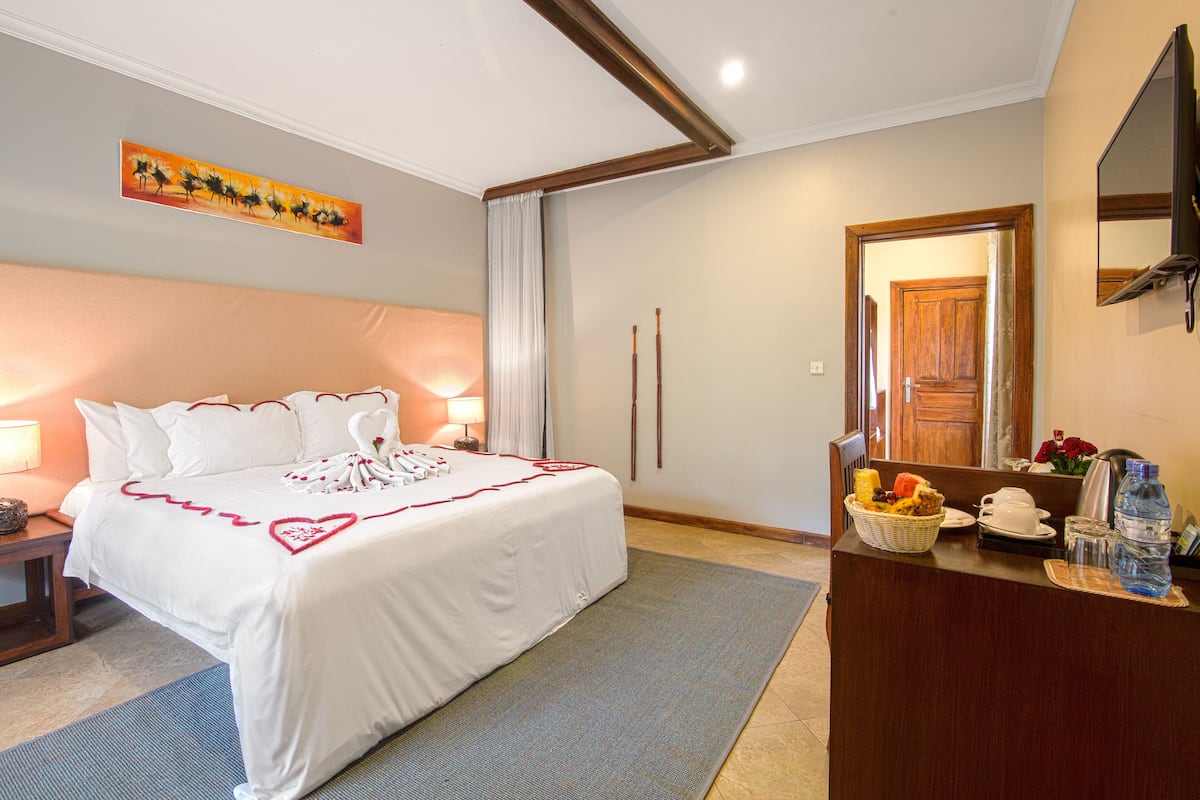 Una habitación de hotel con una cama grande, un escritorio con una cesta de frutas, una botella de agua y un espejo.