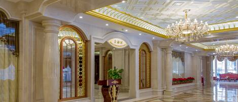 A luxurious lobby with a checkered floor, ornate columns, and a grand chandelier.