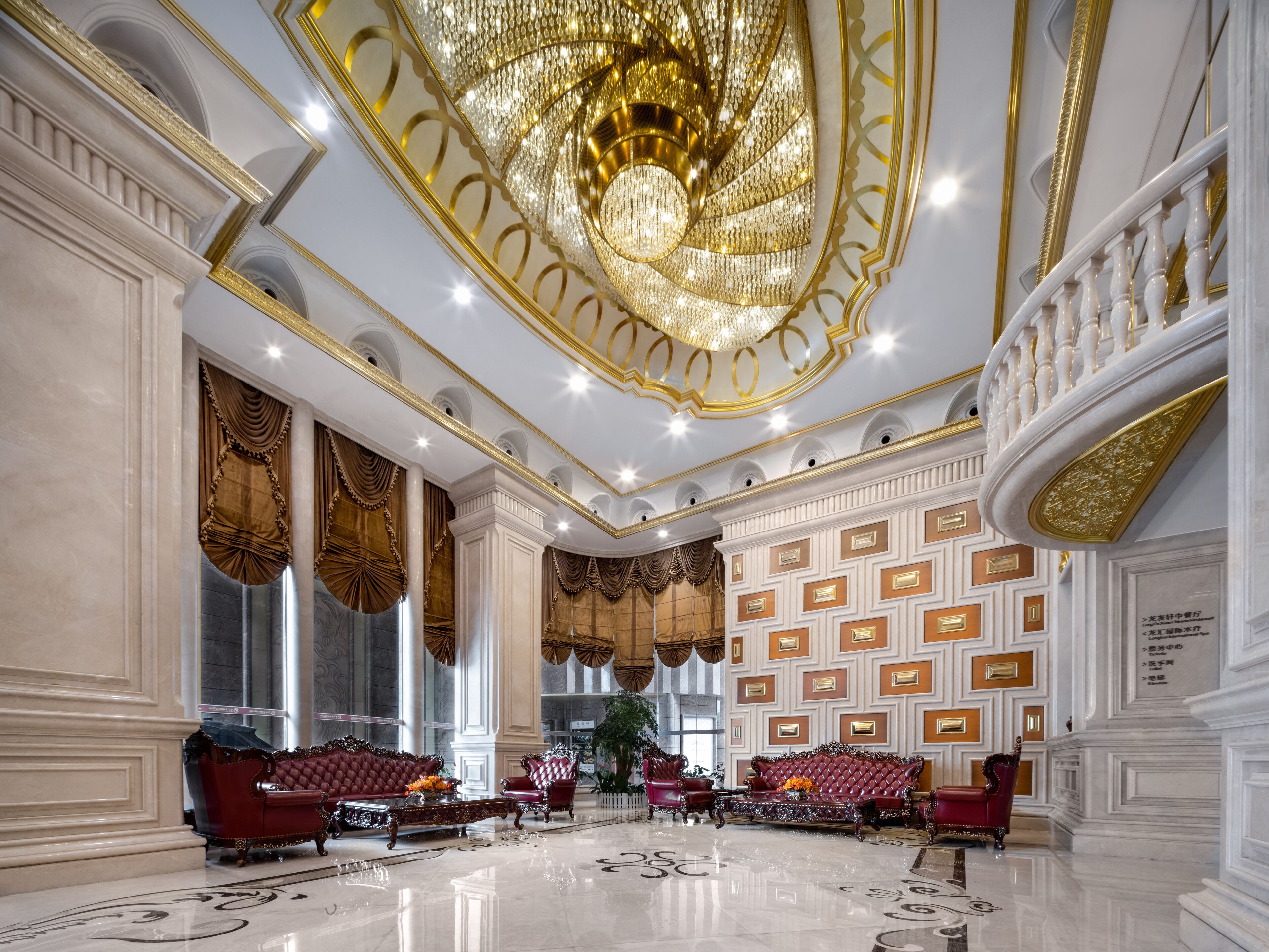 Un hall d’entrée luxueux, agrémenté de lustres somptueux, d’élégants canapés rouges et d’un grand escalier.