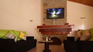 Una sala de estar con dos sofás negros, una mesa de centro de madera y un televisor de pantalla plana montado en una pared de ladrillo.