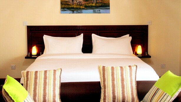 Una habitación de hotel con una cama grande, dos lámparas de noche y un cuadro de elefantes en la pared.