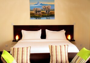 Una habitación de hotel con una cama grande, dos lámparas de noche y un cuadro de elefantes en la pared.