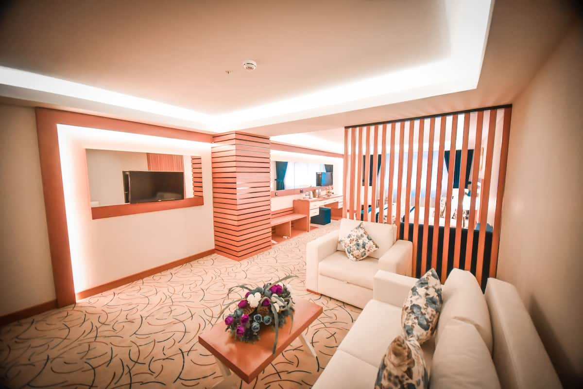 A modern living room with a sofa, a coffee table with flowers, a TV, and a kitchen area with a wooden partition.