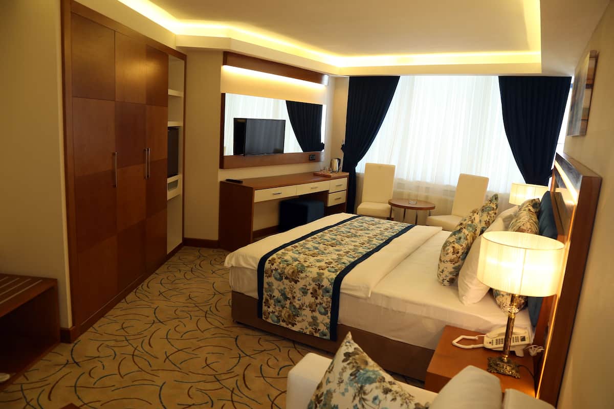 A hotel room with a bed, bedside table, lamp, and a desk with a chair.