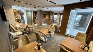 A modern hotel lobby with multiple seating areas, including tables and chairs, and a large window providing a view of the outside. - Sarikamis Aras Otel (Sarikamis)