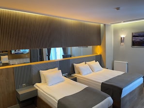 Moderni hotellihuone, jossa on kaksi sänkyä, suuri peili, taulutelevisio ja näkymä ulos.