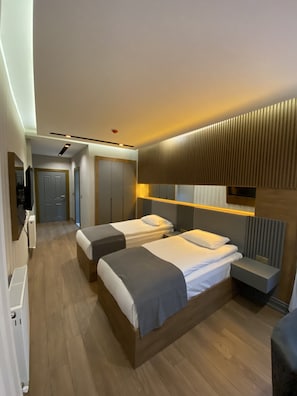 Moderni hotellihuone, jossa on kaksi sänkyä, pieni työpöytä ja sisäänrakennettu vaatekaappi.