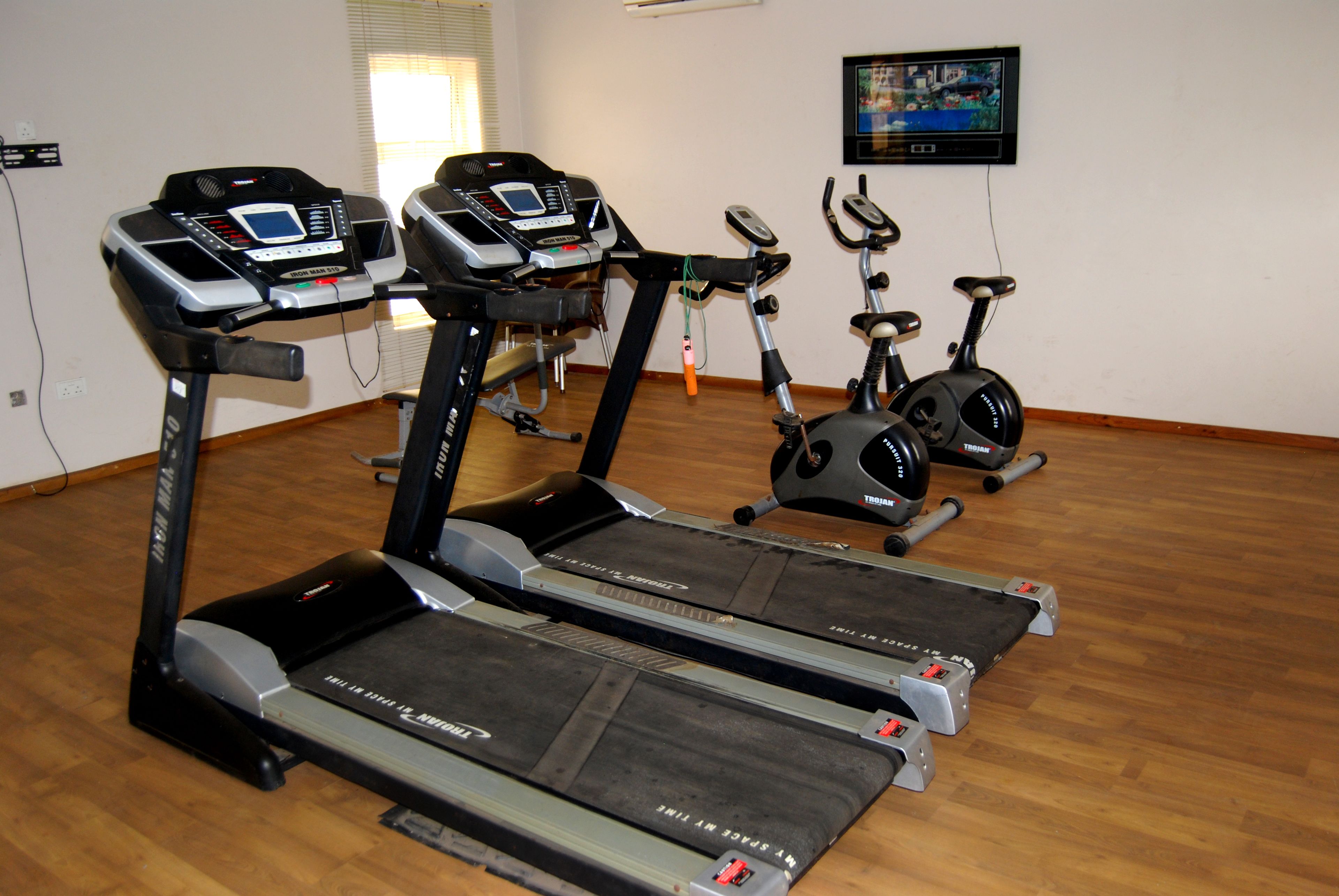 A gym with treadmills, stationary bikes, and a TV on the wall.