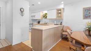 A modern kitchen with white cabinets, a central island, and a dining area with a wooden table and chairs.
