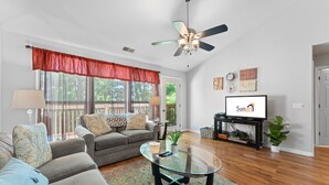 A living room with a sofa, a glass coffee table, a ceiling fan, and a television displaying a rental sign. - Heavenly Hideaway 2 Bedroom Condo by RedAwning (Branson West)