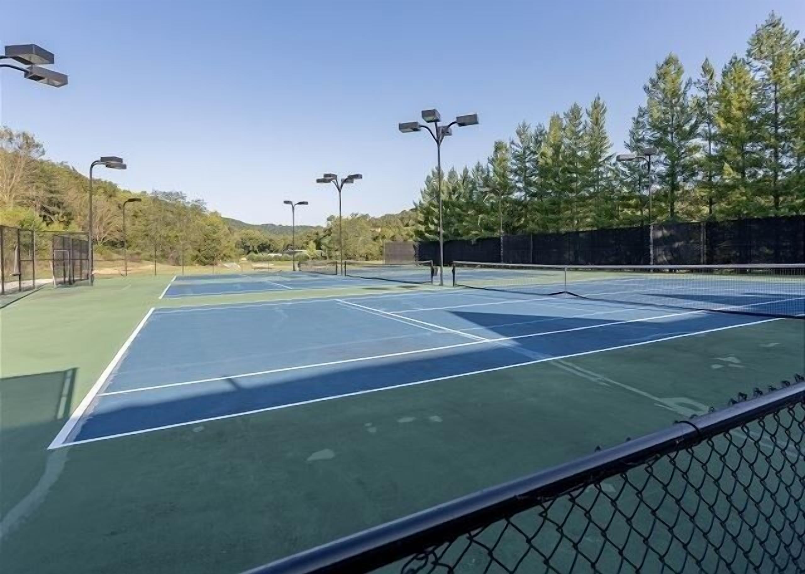 Un court de tennis comprenant plusieurs terrains, entouré d’arbres et d’une clôture.