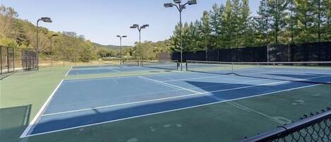 Un court de tennis comprenant plusieurs terrains, entouré d’arbres et d’une clôture.