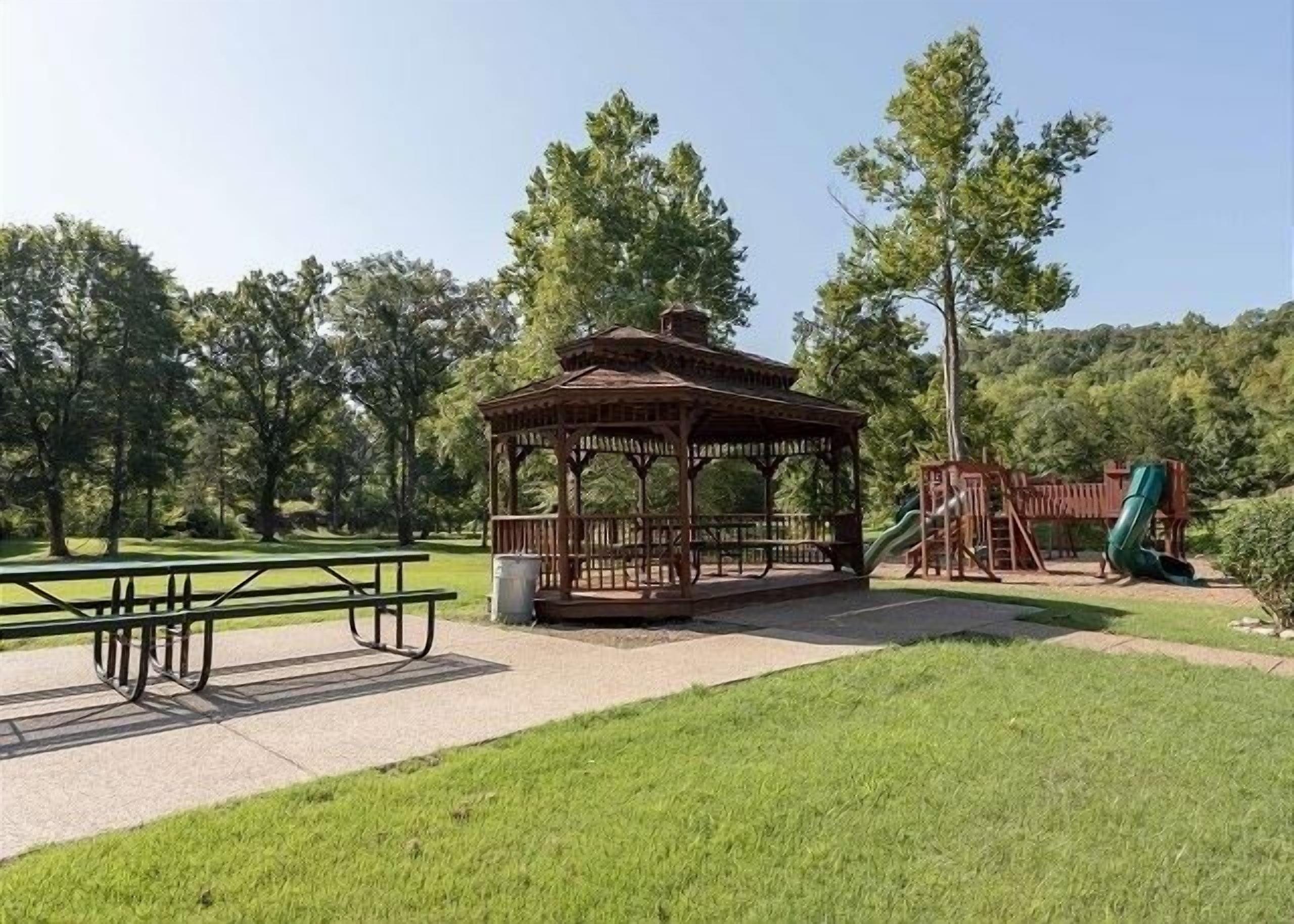 A gazebo, picnic table, and playground in a park.
