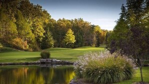 A serene golf course with a pond, surrounded by trees and a stone wall. - Heavenly Hideaway 2 Bedroom Condo by RedAwning (Branson West)