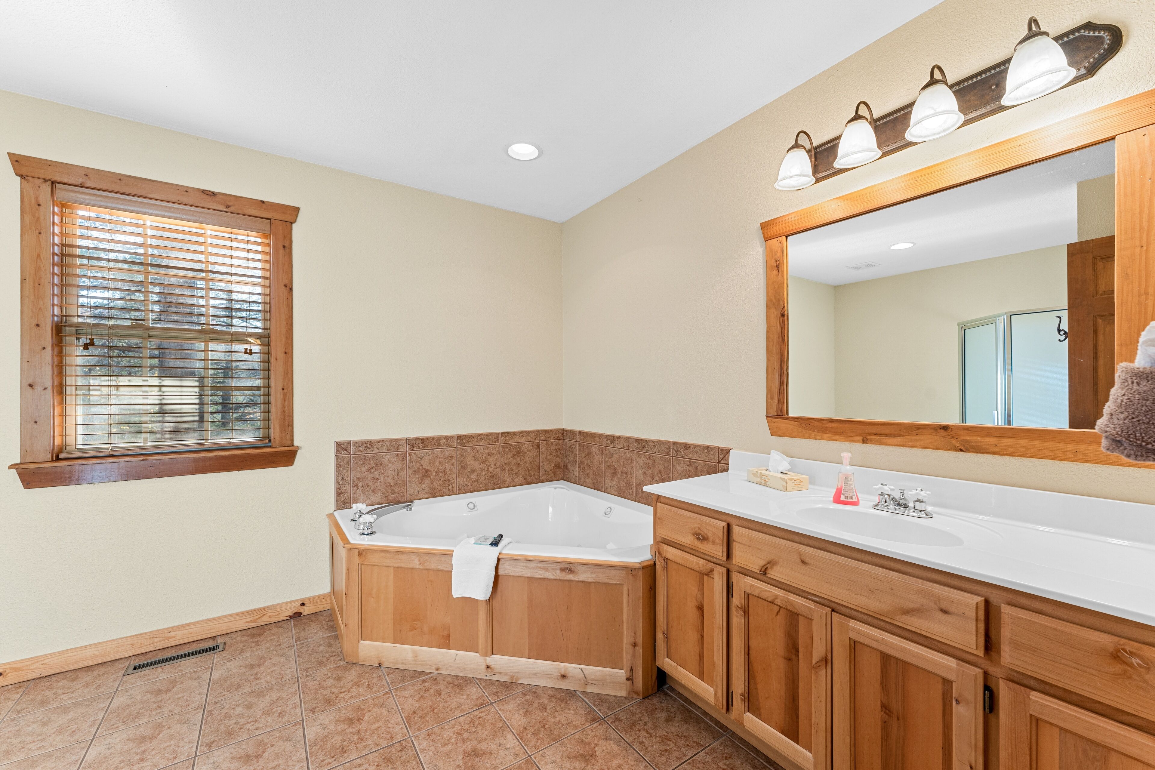 Une salle de bain avec une grande baignoire, des meubles en bois, un lavabo blanc et un miroir avec éclairage intégré.