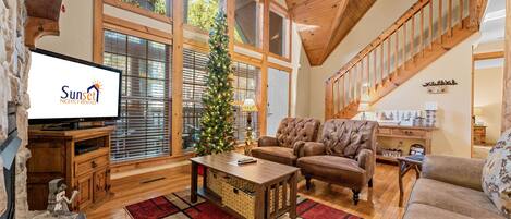 Un salón amplio con chimenea, ventanas grandes, un árbol de Navidad y una escalera.