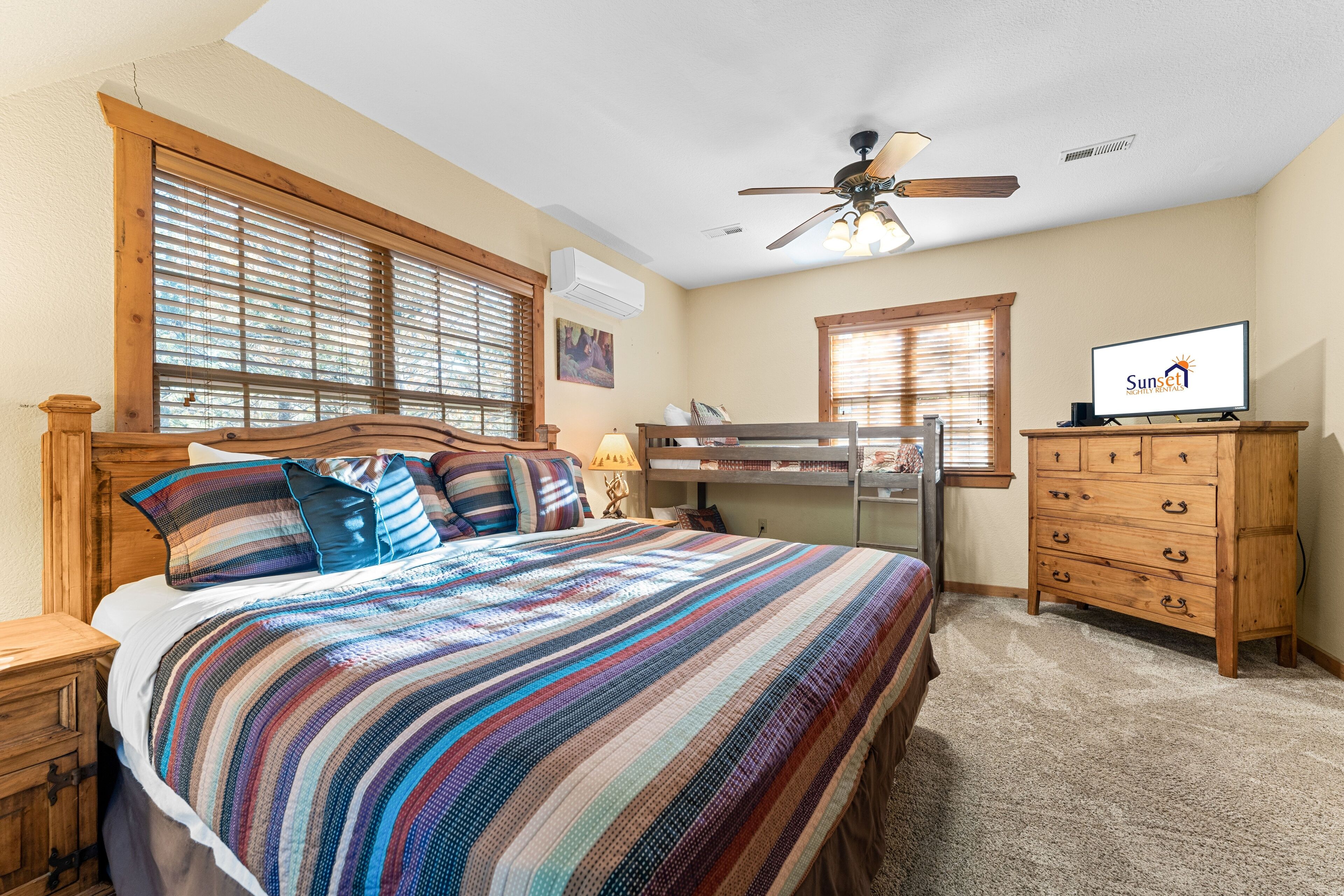 A bedroom with a bunk bed, a wooden dresser, a television, and a ceiling fan.
