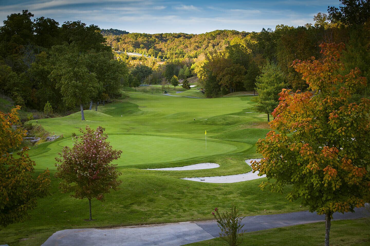 A golf course with a clear view of the green, sand bunkers, and surrounding trees.