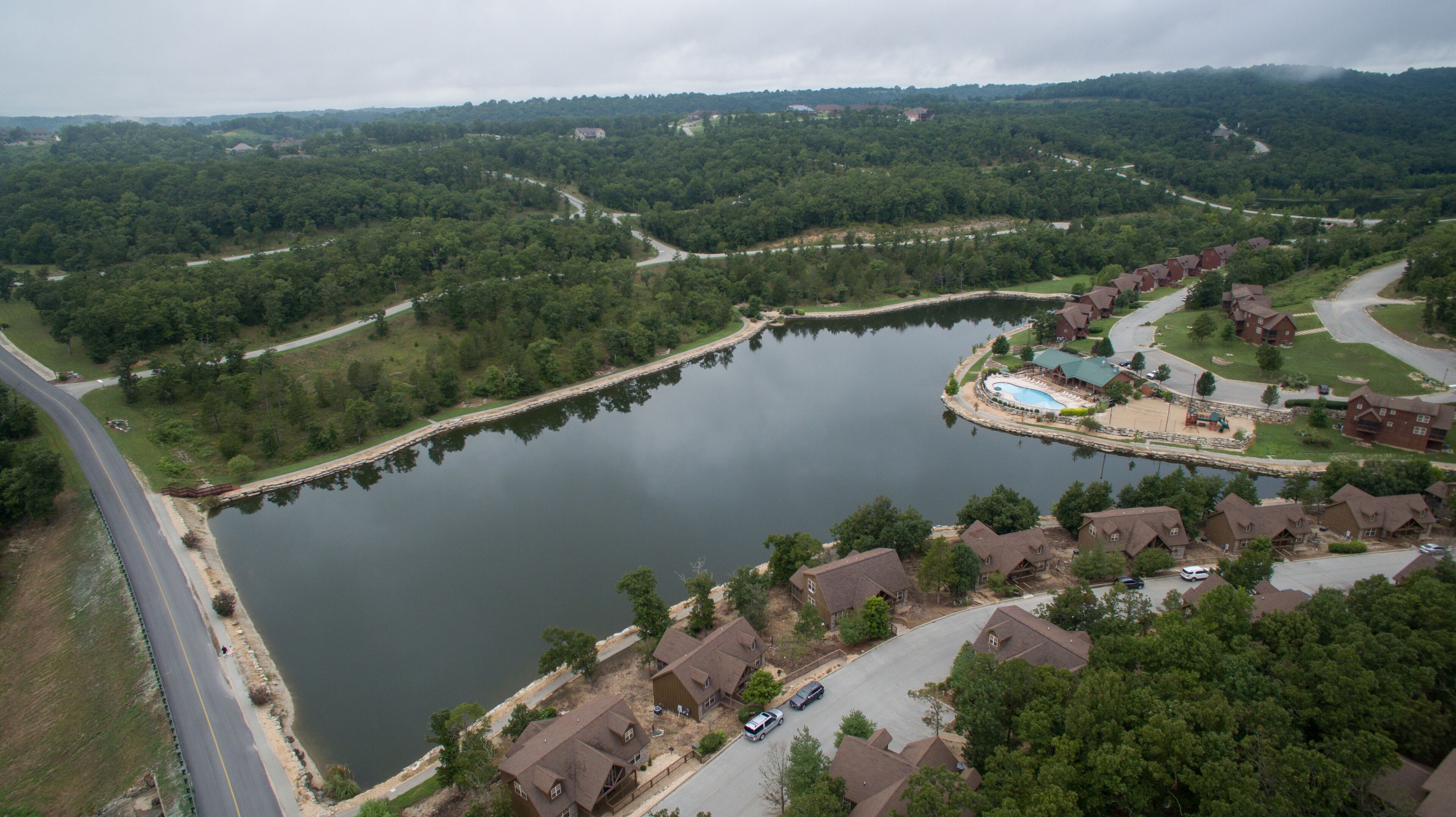 An aerial view of a residential area with a large lake, houses, and a swimming pool.