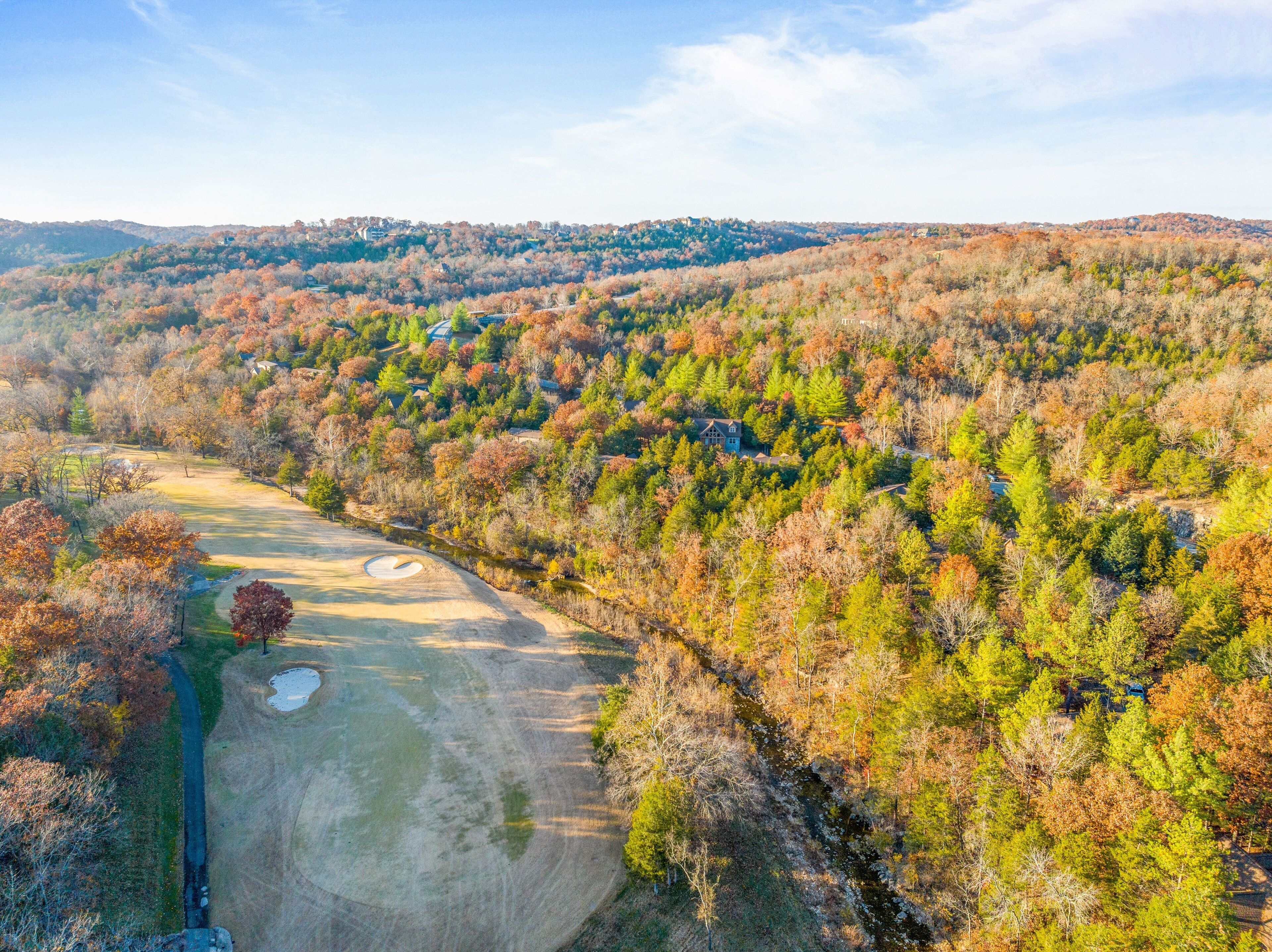 A golf course with a pond, surrounded by autumn-colored trees and hills in the background.