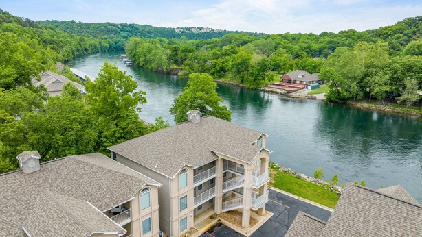 A multi-story building with a parking lot and a river in the background. - Fort Taneycomo 2 Bedroom Condo by RedAwning (Branson)