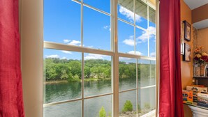 A room with a large window overlooking a river, a white fireplace, and a shelf with various items. - Fort Taneycomo 2 Bedroom Condo by RedAwning (Branson)