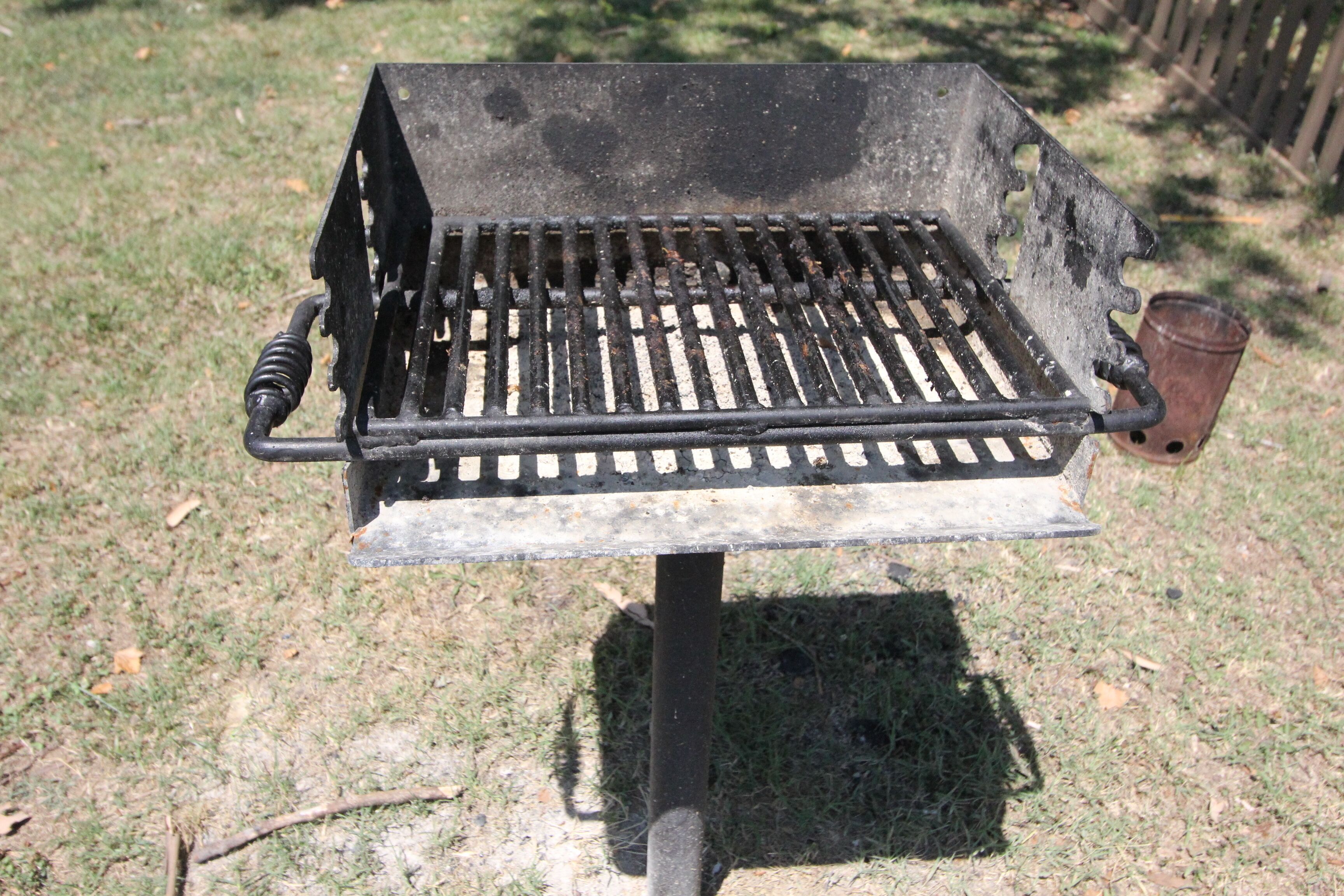 Una parrilla portátil con rejilla calientapiedras, asa y estructura de metal.