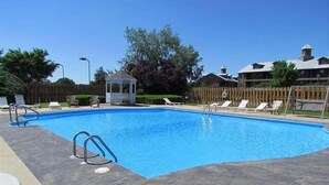 En rektangulär swimmingpool med ett kaklat poolområde, omgiven av solstolar och en pergola.