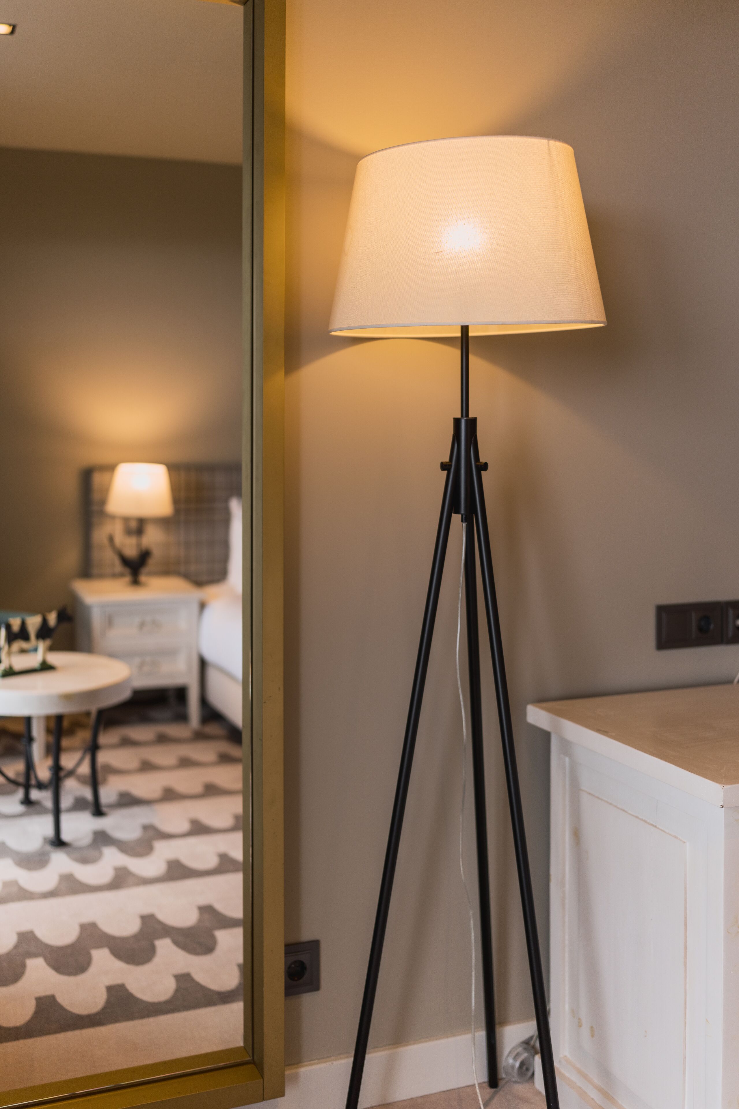 A modern hotel room with a standing floor lamp, a round table, and a bed with a headboard.