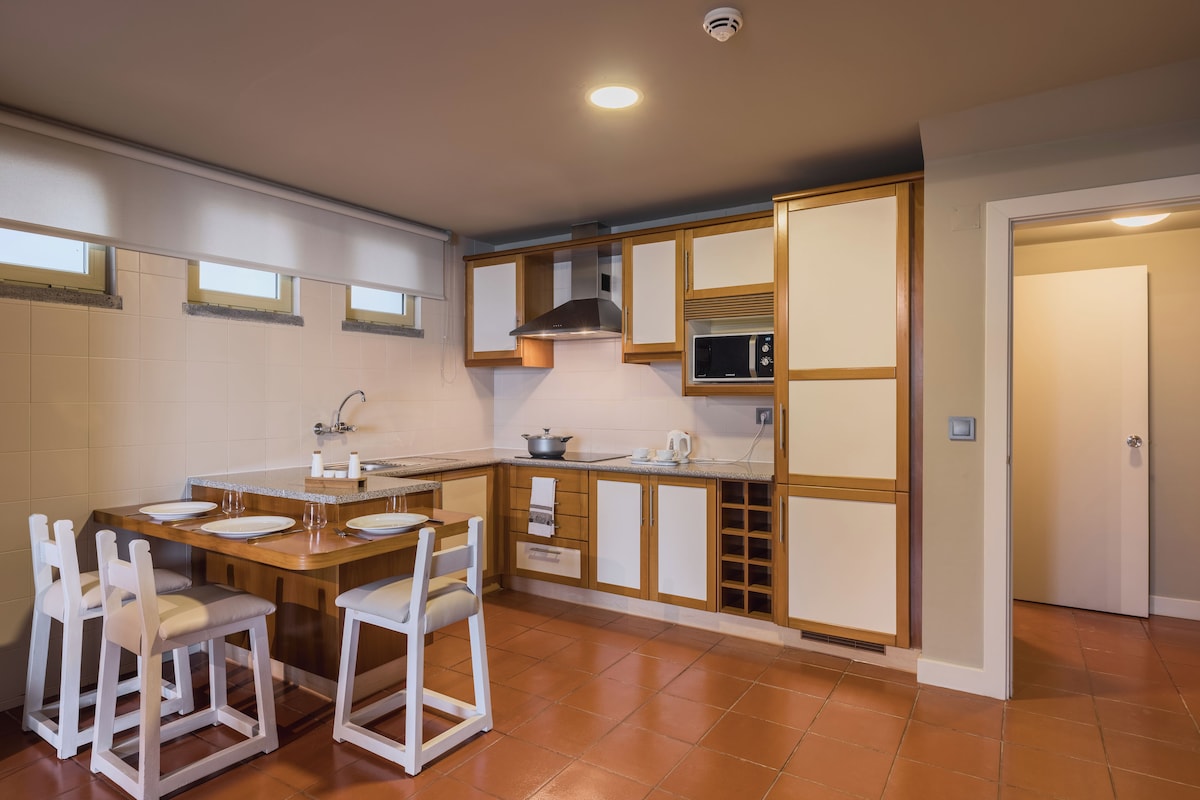 A compact kitchen with a central island, white chairs, and a microwave.