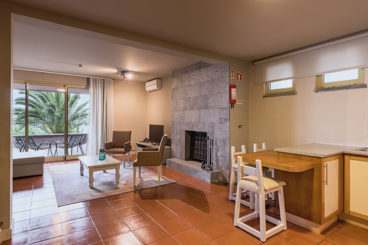 Een moderne woonkamer met een open haard, een eethoek met een keukenbar, en een balkon met buitenmeubilair.