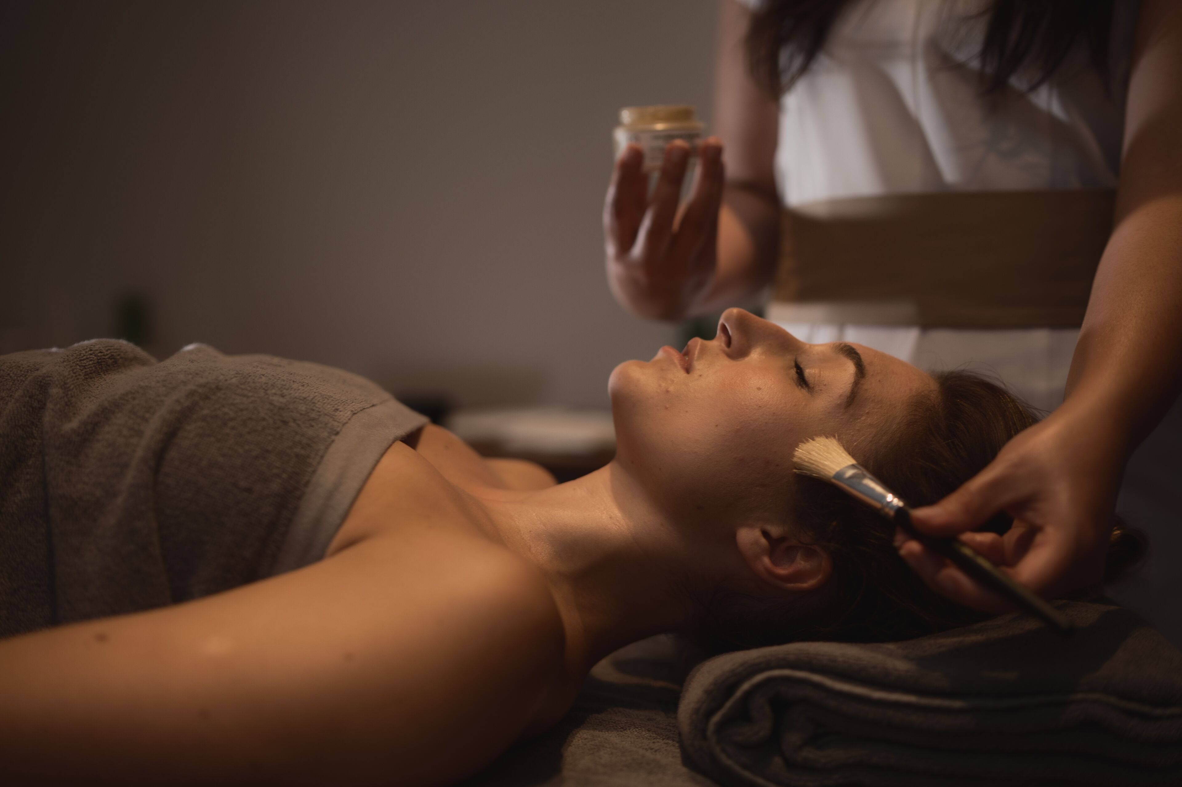 Une personne est allongée et une autre personne lui applique une substance sur le visage.