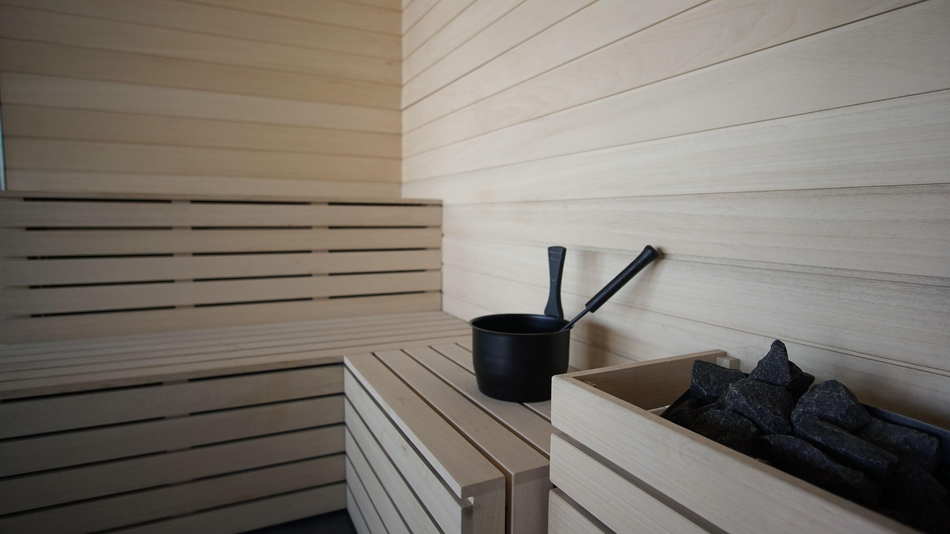 A sauna room with wooden slats on the walls, a black pot, and a wooden bench.