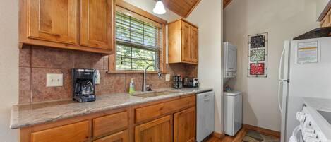 Una cocina con armarios de madera, cafetera, lavamanos y refrigerador.