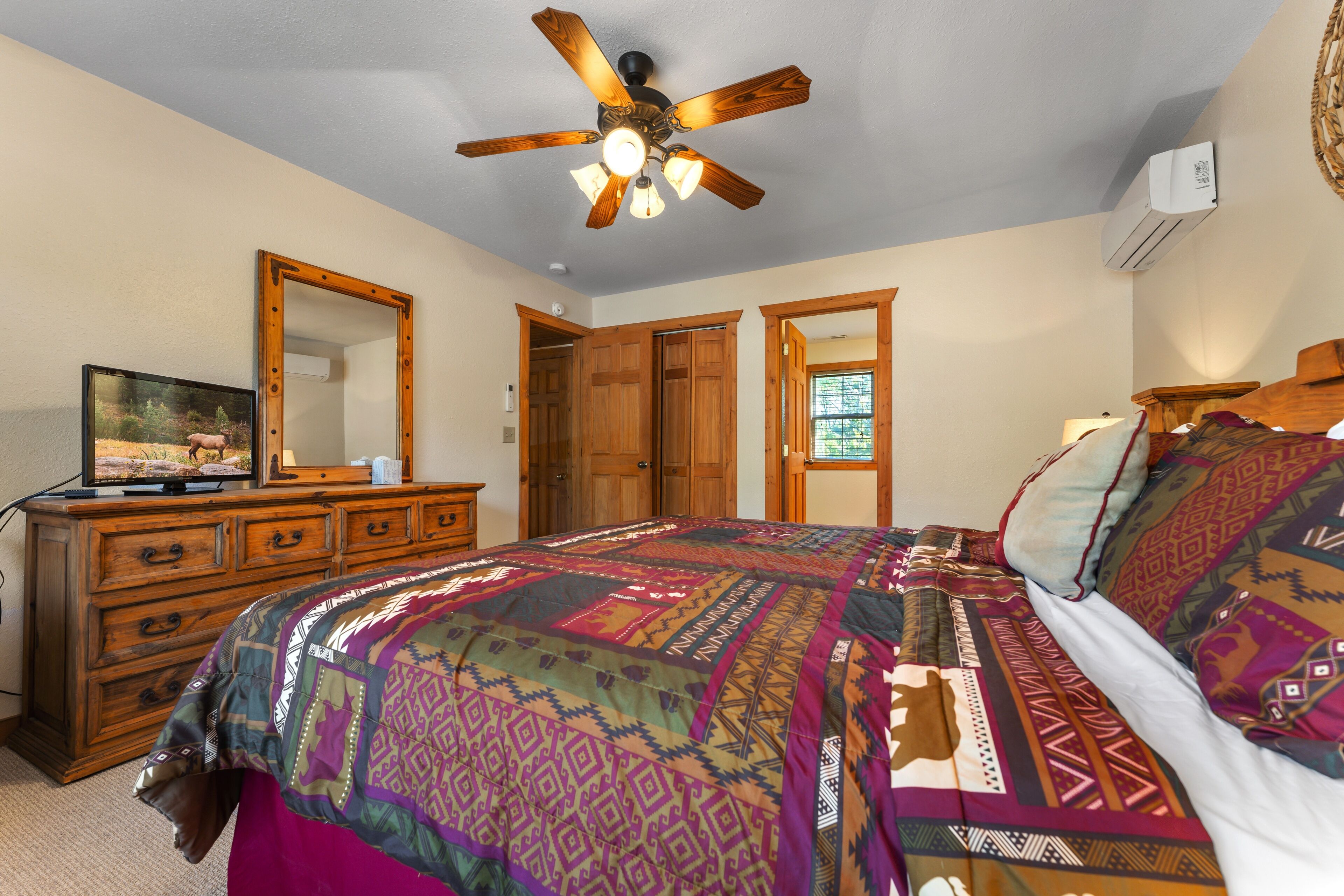 A bedroom with a bed, a ceiling fan, a dresser, a mirror, and a window.