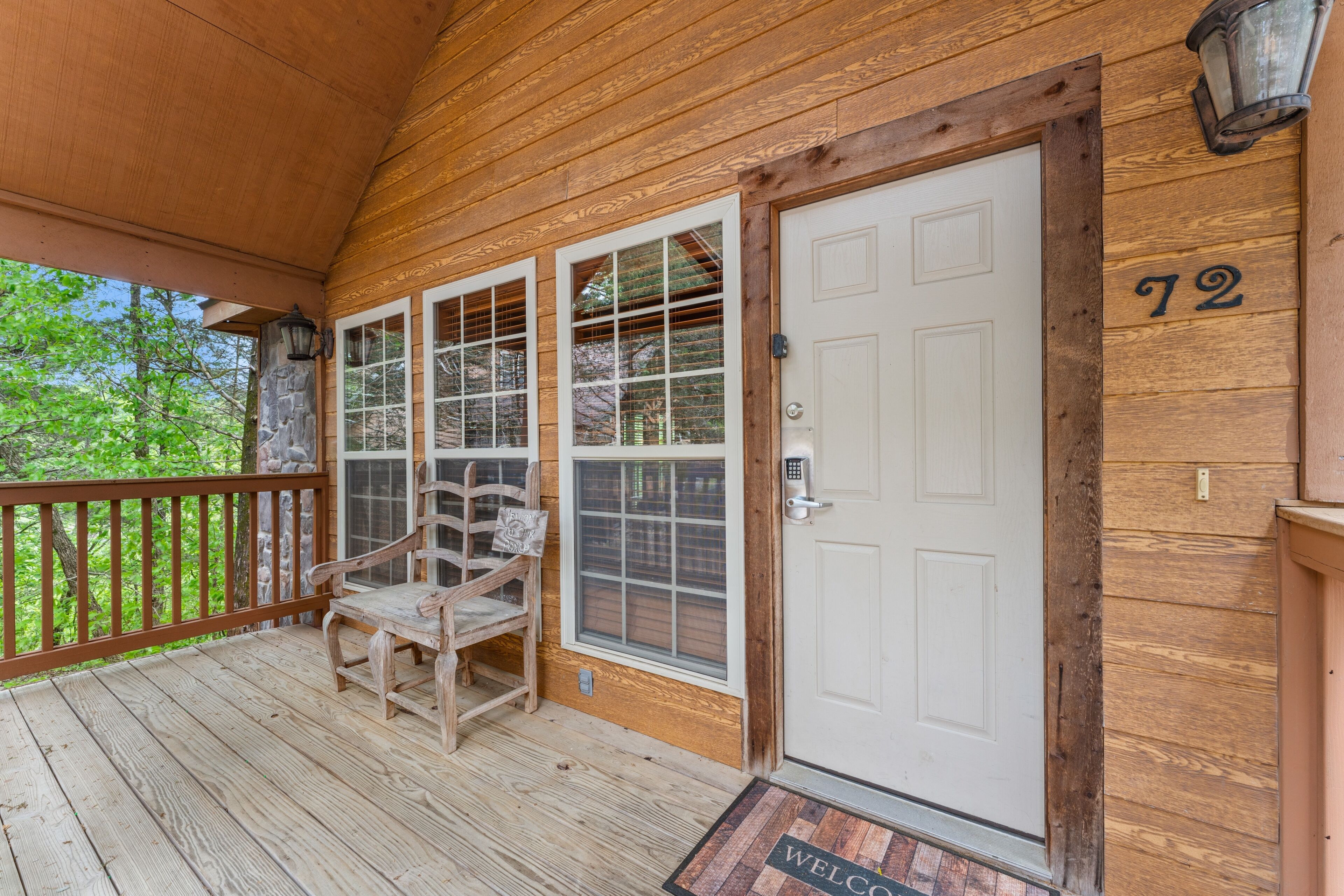 A wooden porch with a bench, a door with a number '72' above it, and a welcome mat at the entrance.