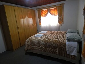 A bedroom with a bed, a wardrobe, and a window with curtains. - Apartamento De Luxe Gramado (Gramado)