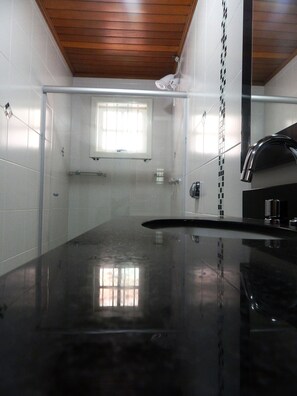 A modern kitchen with a glossy black countertop, white tiled walls, a wooden ceiling, and a window providing natural light. - Apartamento De Luxe Gramado (Gramado)
