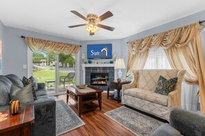 A living room with a fireplace, a ceiling fan, and a television displaying a logo. - Dream Weaver 2 Bedroom Condo by RedAwning (Branson)